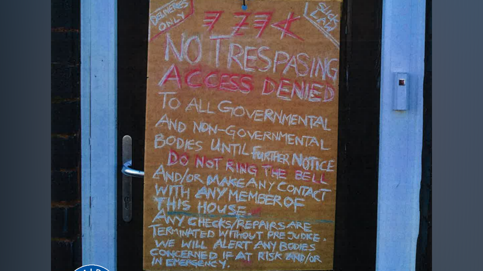 A large sign on a front door which reads "no trespasing, access denied to all governmental and non-governmental bodies until further notice. Do not ring the bell and/or make contact with any member of this house. Any checks/repairs are terminated without prejudice. We will alert any bodies concerned if at risk and/or in emergency"