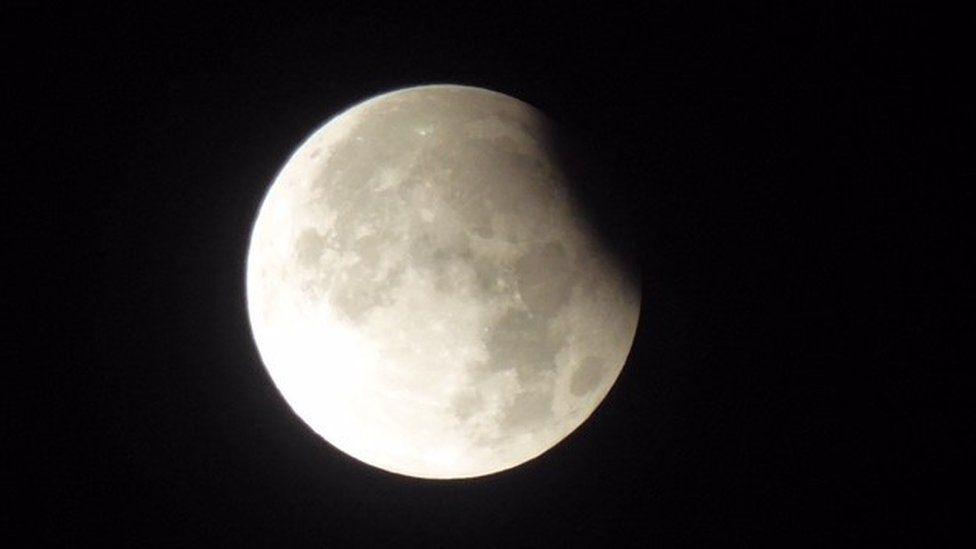 Bright white moon against black sky with shadow over small part of the moon's surface