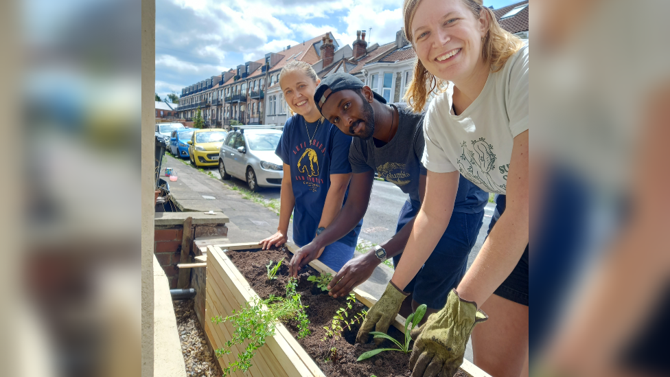 Three residents of Camerton Road in Easton midway through planting some plants in a trough. All three of them are looking at the camera and smiling