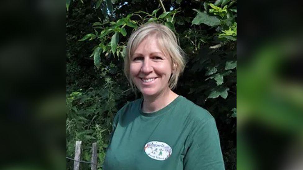 Nicky Lewis, the co-owner and manager of Keepers Gate Forest School. She has blonde hair and wears a forest-green shirt. 