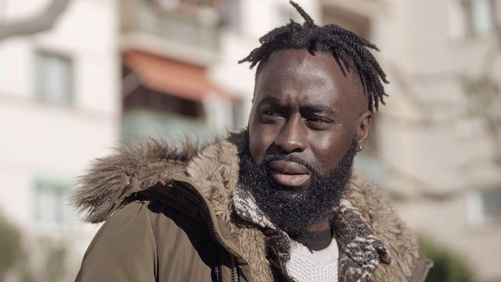 Menka Gomis wearing a winter coat in France. He has a beard and short dreadlocks.