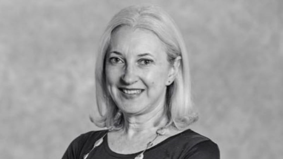 Black and white photo of Catherine Finnegan. She has shoulder length hair, wears earrings, a necklace, a black top and smiles at the camera.