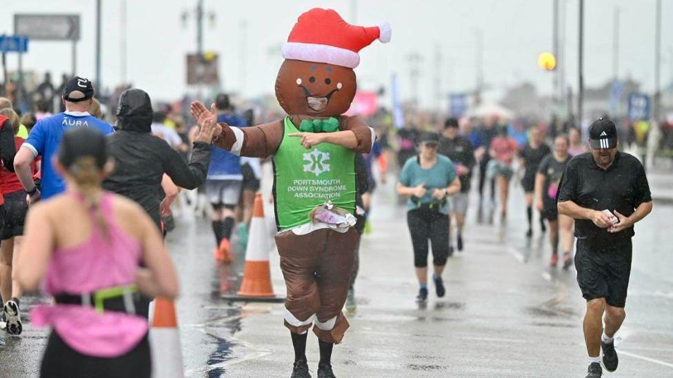Runners during the race with one person in the middle dressed as a gingerbread man with a santa hat on his head.