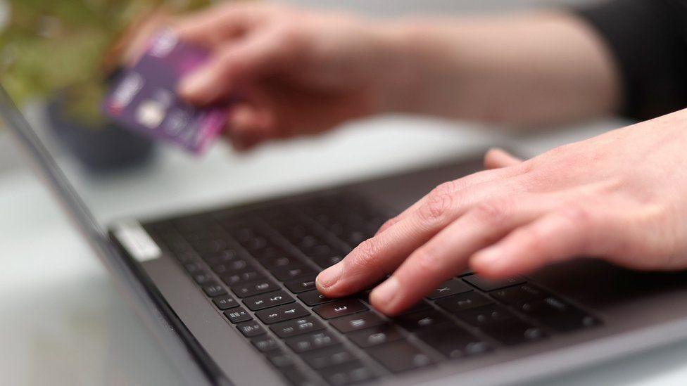 Someone using a laptop while holding their debit card