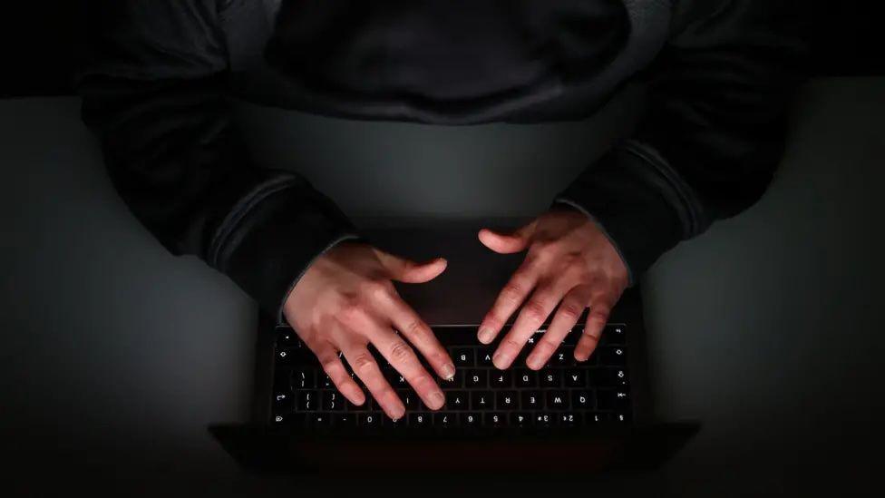 An aerial view of a pair of hands hovering over a black laptop keyboard. the person is wearing a black long-sleeve top and the desk below is also dark.