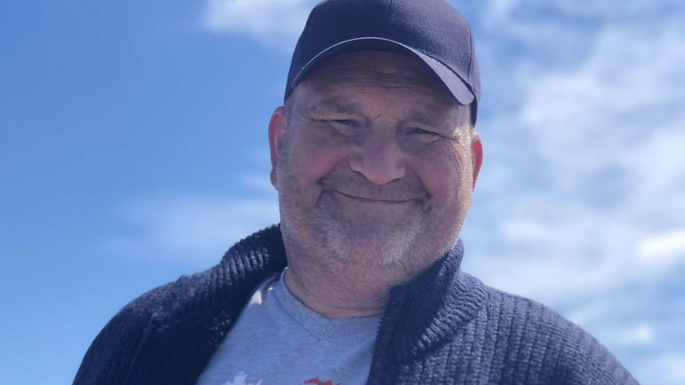 A man in a blue baseball cap, grey T-shirt and dark blue cardigan