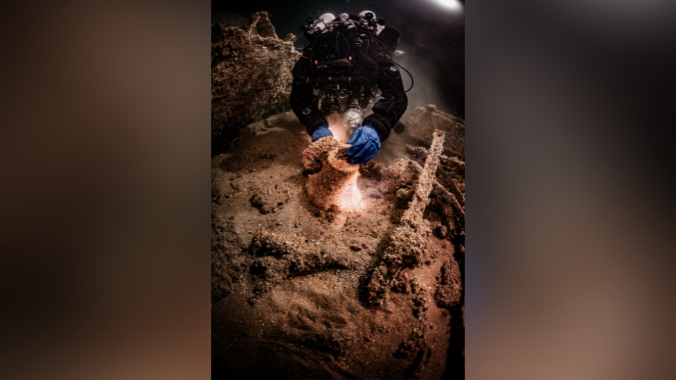 A diver inspecting a warships bell in a shipwreck 