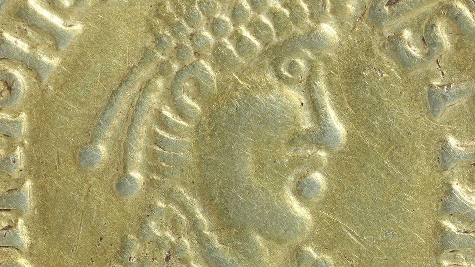 A close-up of an Anglo-Saxon gold coin. It shows an attempt to replicate the face of a Roman emperor in profile and is quite crudely made