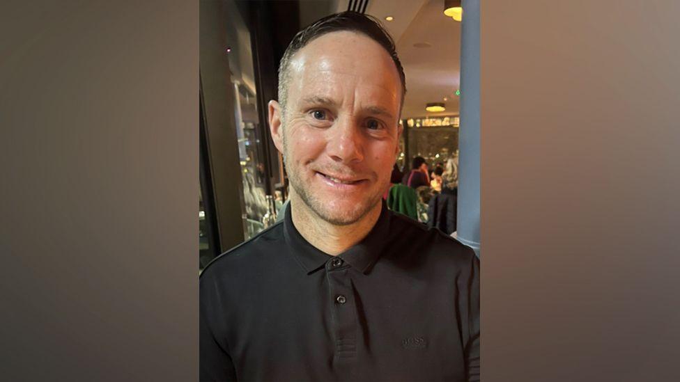 Lee Claydon smiling and wearing a black shirt