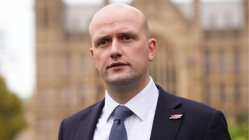 Stephen Flynn, a bald man wearing a dark suit, stands outside parliament 