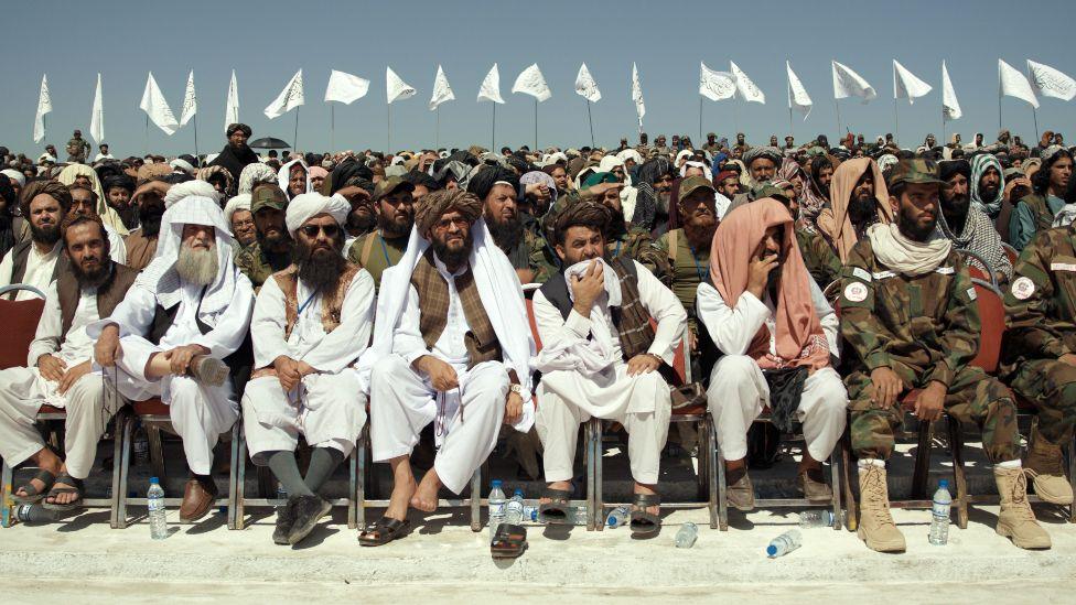 Image from documentary Hollywoodgate, showing the Taliban, sitting in a row, in front of a crowd of people