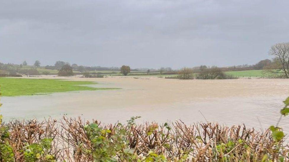 Flood water spans fields with small areas of green grassy banks either side