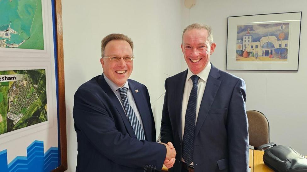 Charles Woodgate (left) shakes hands with Conservative opposition leader Trevor Bartlett (right) after defecting to the Conservatives from Labour