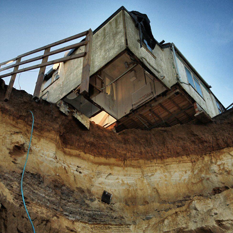 View looking upwards from the beach to the house overhanging the cliff edge