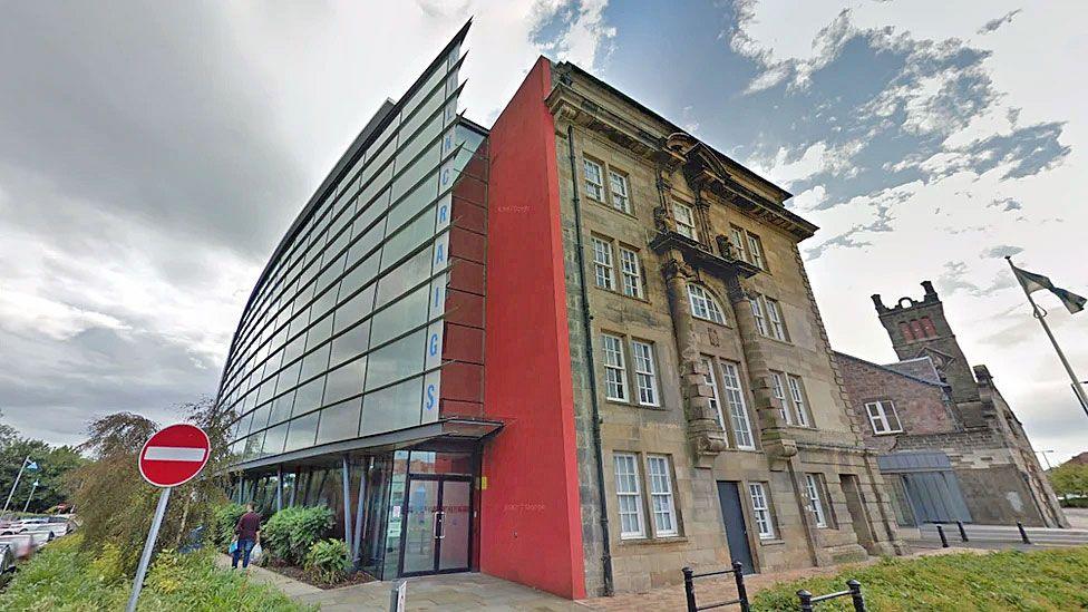 A council headquarters with stone on one side and glass panels on the other beneath an ominous sky