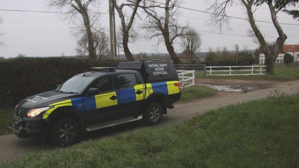 Royal Navy Bomb Disposal truck parked on a rural road with white fencing and a house seen in the distance.