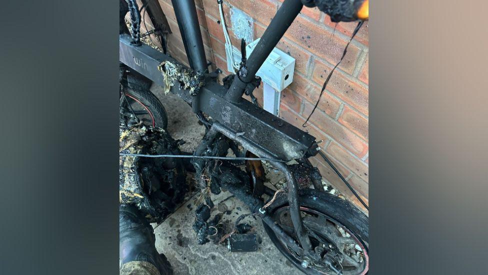 A burnt out ebike standing next to a brick wall