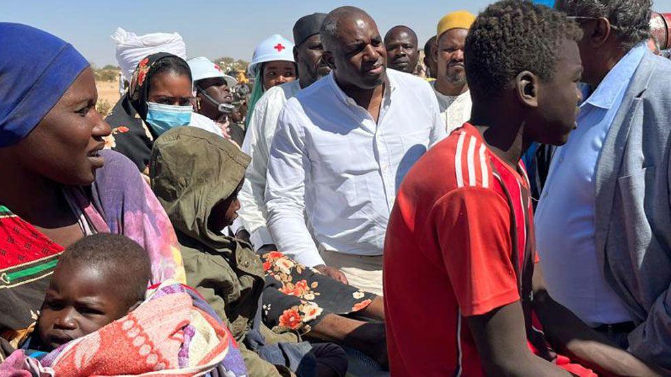 David Lammy in a white amidst a crowd of Sudanese people newly arrived in Chad and aid workers. 