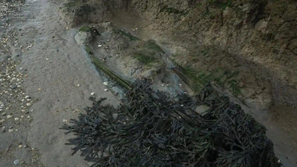 The outline of a coffin in a wet muddy area.