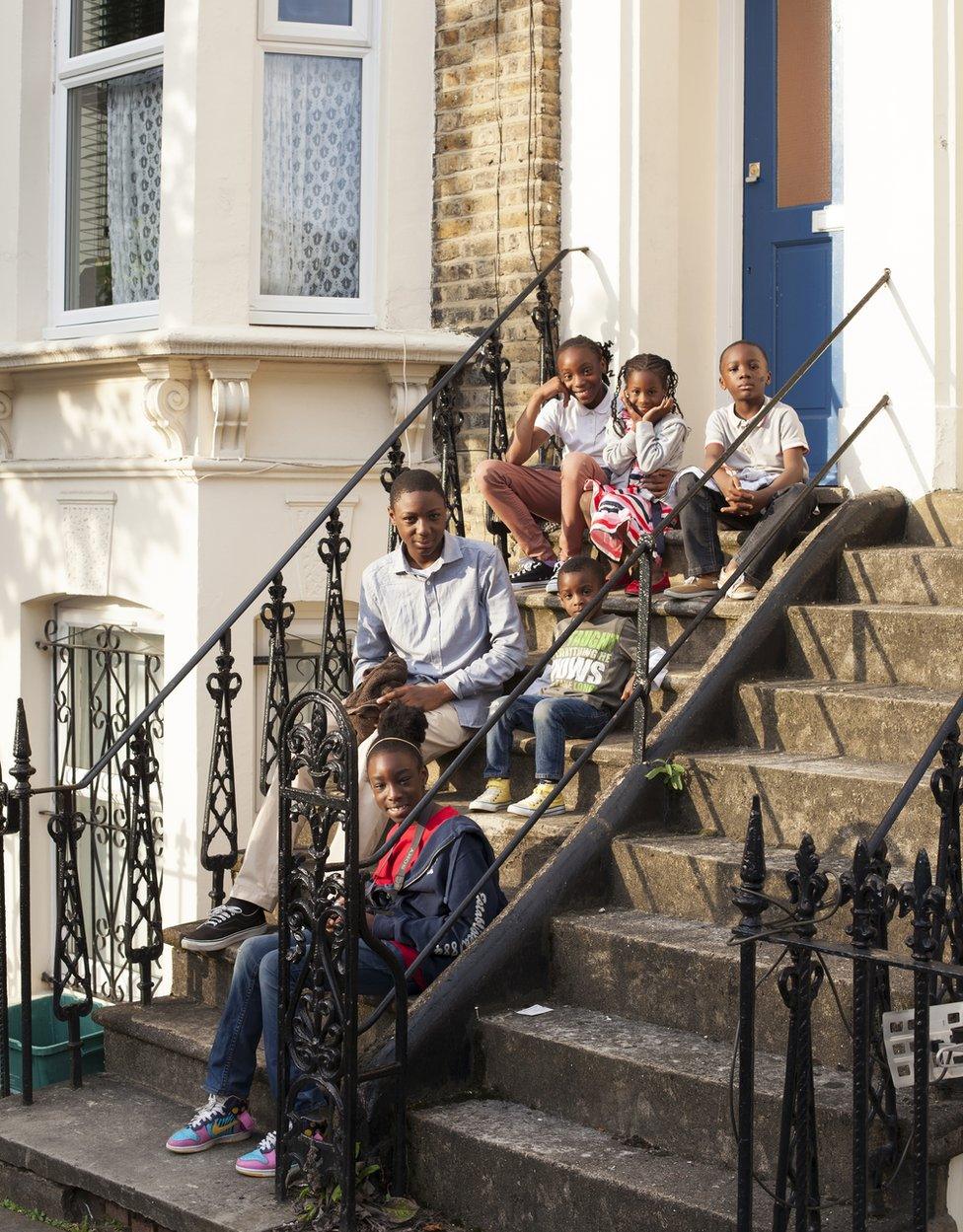 A group of children sit outside their house