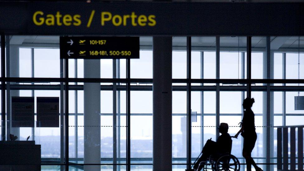 A wheelchair user and companion look out at planes on a runway