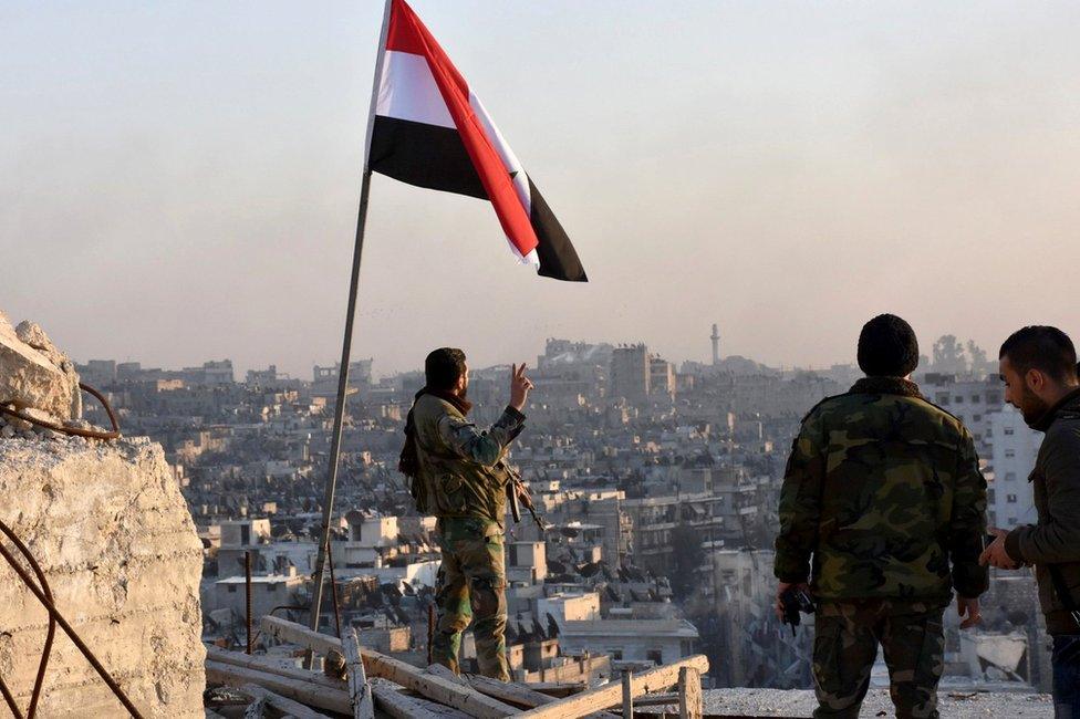 A Syrian government soldier makes a gesture under a Syrian national flag in Aleppo (28 November 2016)