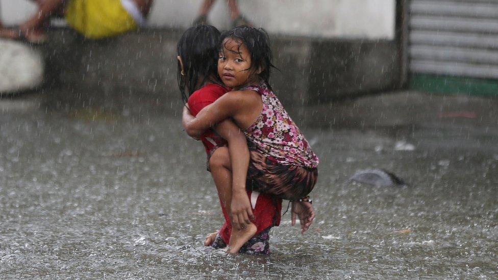 A Filipino girl is carried along a flooded road in suburban Mandaluyong, east of Manila, Philippines, as monsoon downpours intensify while Typhoon Nepartak exits the country on Friday, July 8, 2016