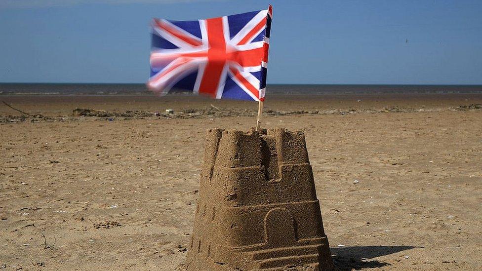 Union Jack flag sits on top of a sand castle on a beach