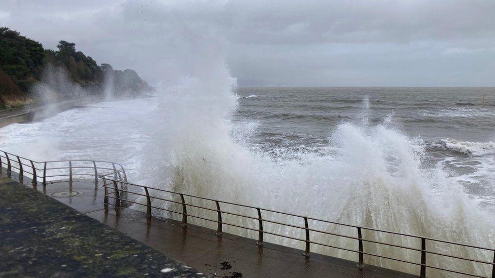 Seafront promenade with metal railings with large waves bursting over the top.