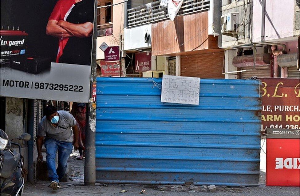 A man ducks to cross a roadblock by RWA during lockdown to curb the spread of coronavirus, at Shastri Nagar, in New Delhi