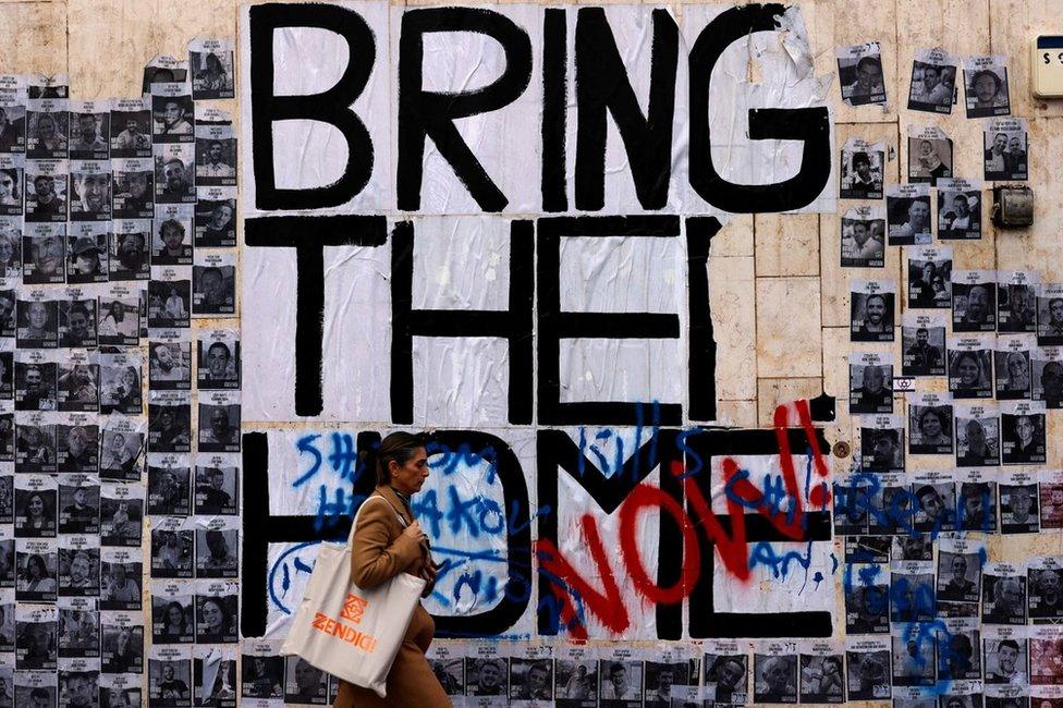 A woman walks past a wall of posters showing hostages taken to Gaza during the 7 October attacks, in Tel Aviv, Israel (24 January 2024)