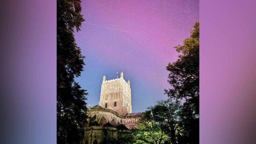 Tewkesbury Abbey framed by trees either side and the purple colours of the Northern Lights in the nightsky beyond