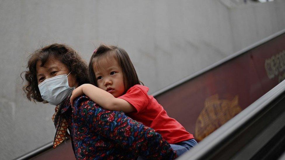 A girl rides on the back of a woman down an escalator at a shopping centre on International Children's Day in Beijing