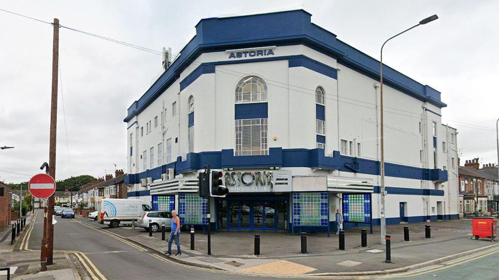 Exterior of the Astoria Bingo Club a large Art Deco former cinema which is painted white with dark blue strips along its roof and above the main door. It is located on a corner site on Holderness Road and Lake Drive 