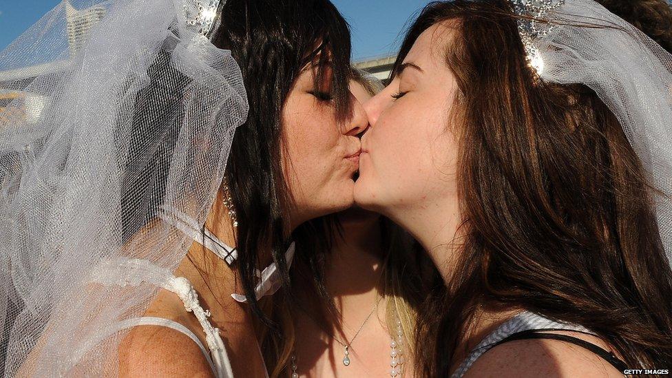 Two young women wearing wedding veils kiss