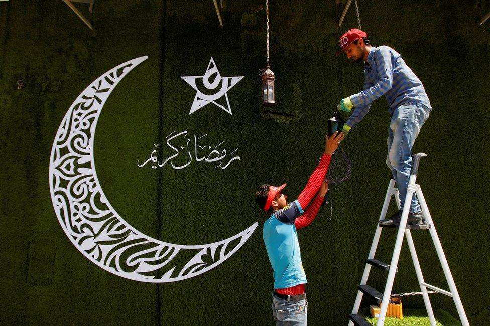 A worker stands on a ladder and hangs a fanous lantern