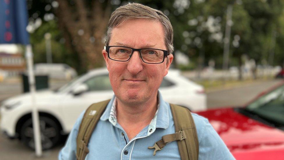 Steve Allen, a man wearing glasses and a blue shirt, stood in front of a car dealership