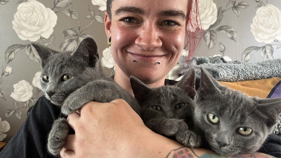 woman holding three sleepy tiny grey kittens