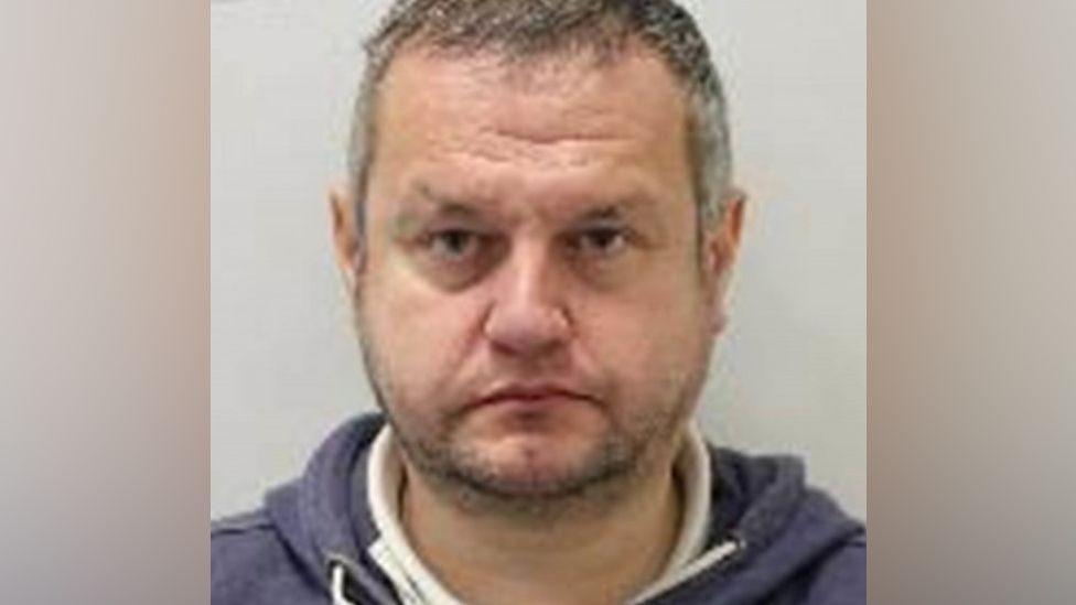 Gareth Viccars is seen in a police custody shot looking at the camera. He has short greying hair and a stubbly beard and moustache. He is wearing a dark blue and white hoodie