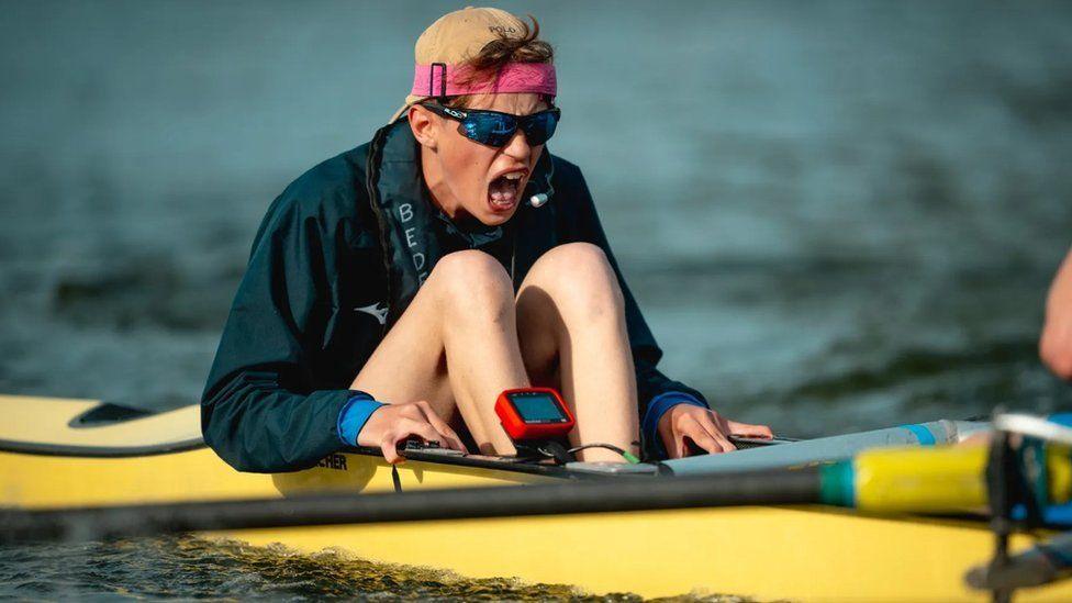 Cox in mid shout on a yellow boat wearing a cap backwards and sunglasses