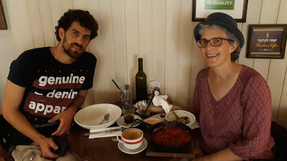 Man in black T-shirt at table across from woman in hat