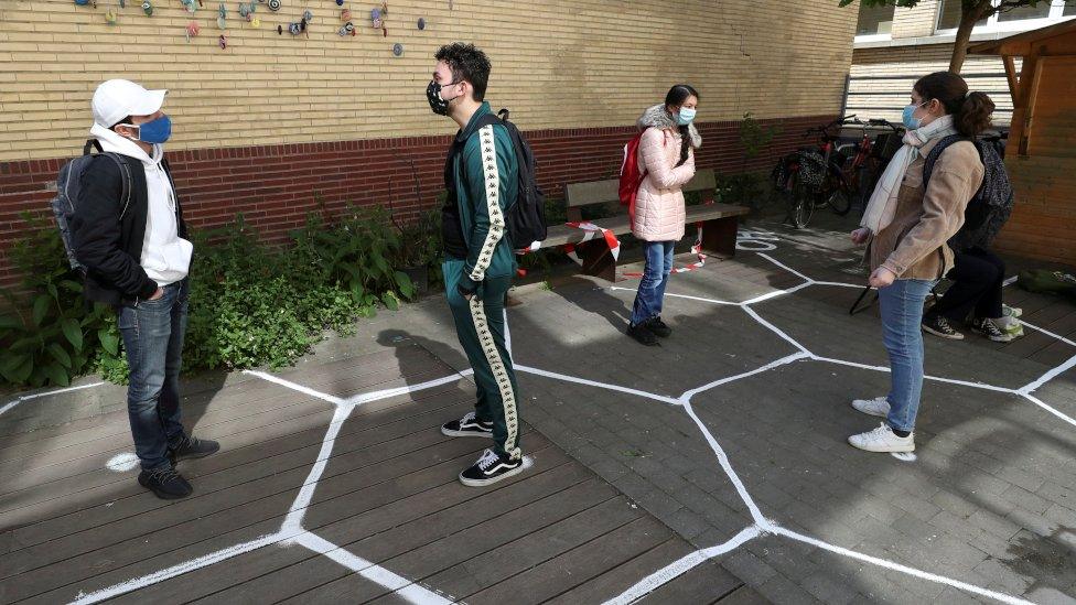 Students stand separately in designated hexagon shapes on the floor