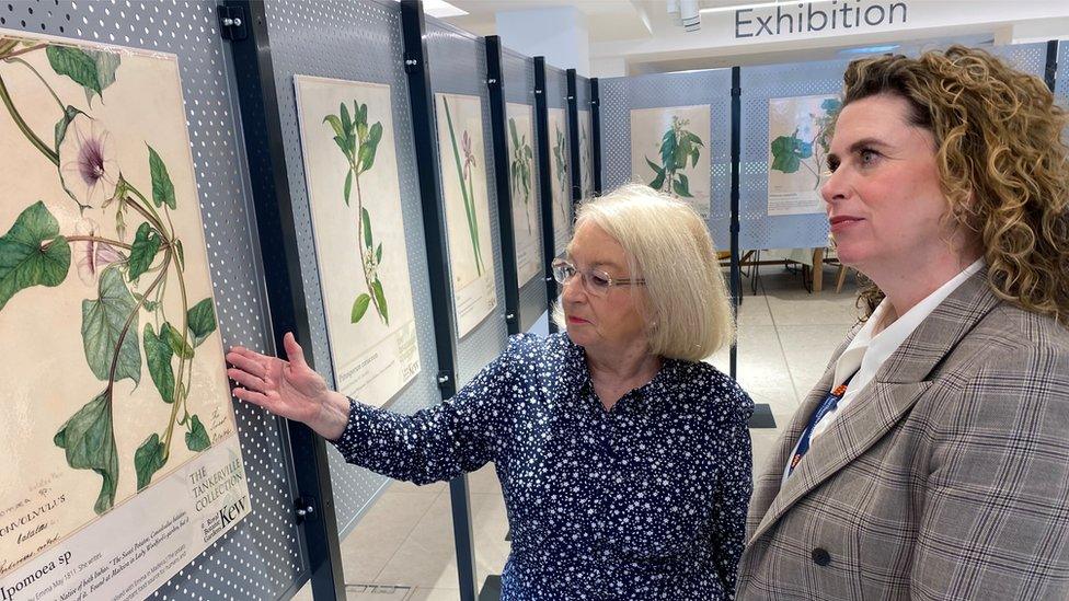 One woman points at pictures of plants as another woman looks on