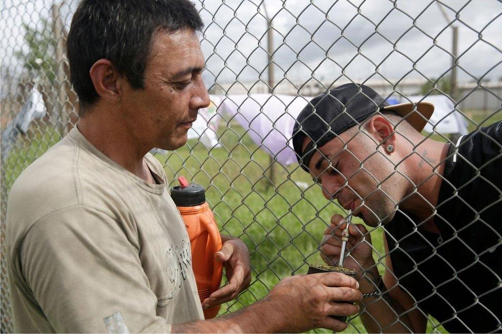 Two men drink a mate tea through a fence at Punta de Rieles jail