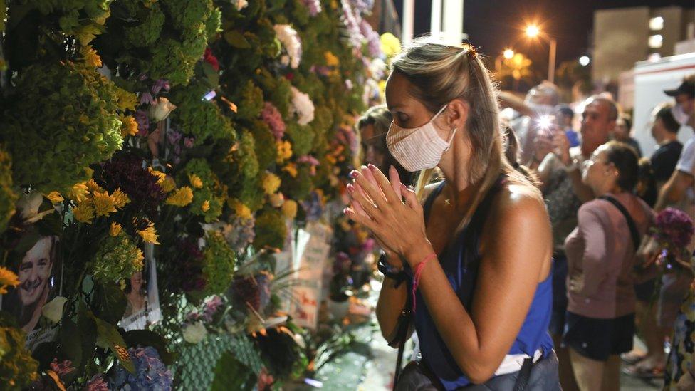 A woman prays as people mourn at the memorial site created in front of the partially collapsed building where the rescue personnel continue their search for victims, in Surfside near Miami Beach, Florida