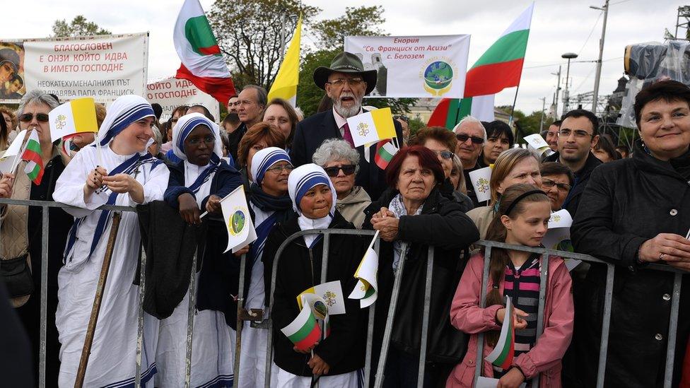 People await the arrival of Pope Francis with flags and banners