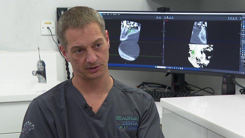 Dr Russell Gidney with dental x-rays on a monitor behind him