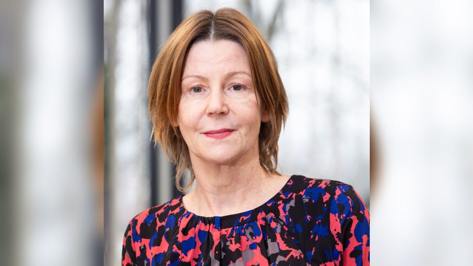 Maria Kane, who has brown hair wearing a calico top coloured red, blue,black and grey