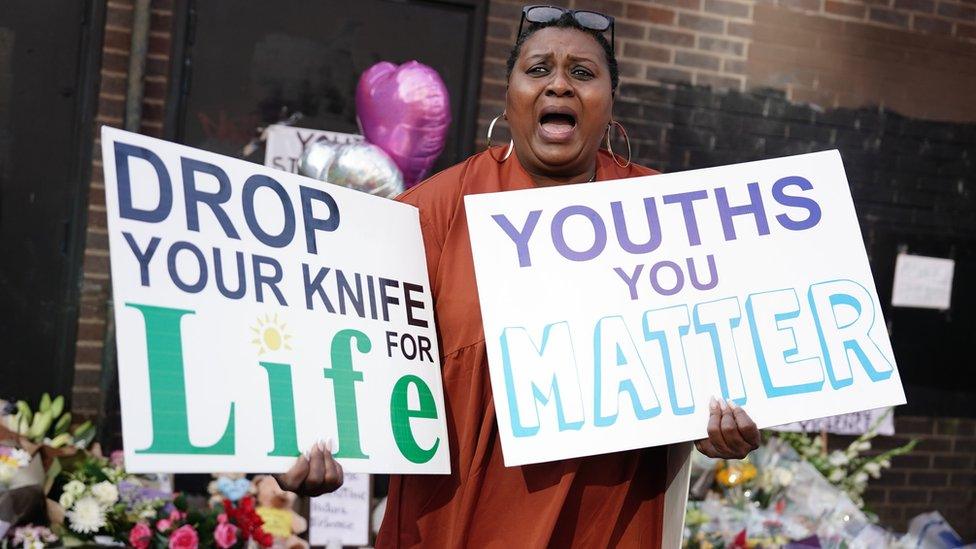 A woman holds two signs that read "drop your knife for life" and "youths you matter" at a protesting against knife crime in Croydon