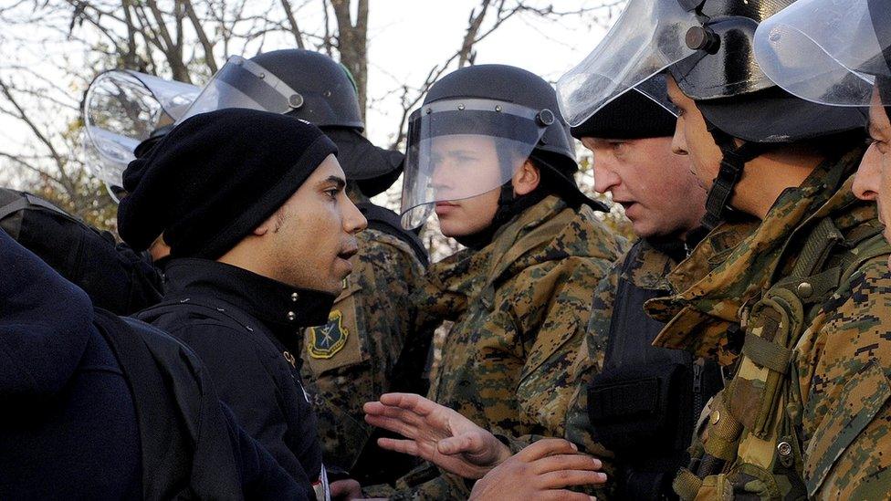 A migrant talks with a Macedonian policeman as he and other migrants wait to cross Greece's border with Macedonia